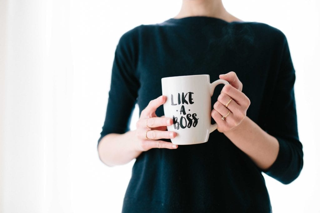 A woman holds a mug that says "like a boss". She is feeling in charge and has used weekly management systems to improve dental front office efficiency
