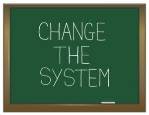 A chalkboard has "change the system" written on it. Weekly management systems are the best way to change dental front office systems.