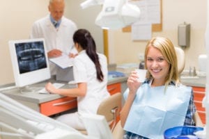 Dental Front Office Systems Benefit The Entire Dental Team. A Dentist Reviews A Patient's Form With a Dental Assistant. A Patient Sits In The Dental Chair Smiling.