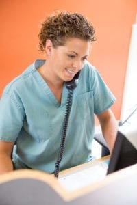 A Dental Front Office Team Member Talks On The Phone As She Schedules A New Patient