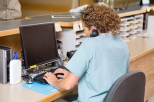 A dental front office team member holds the phone to her ear and schedules a new patient on the computer.