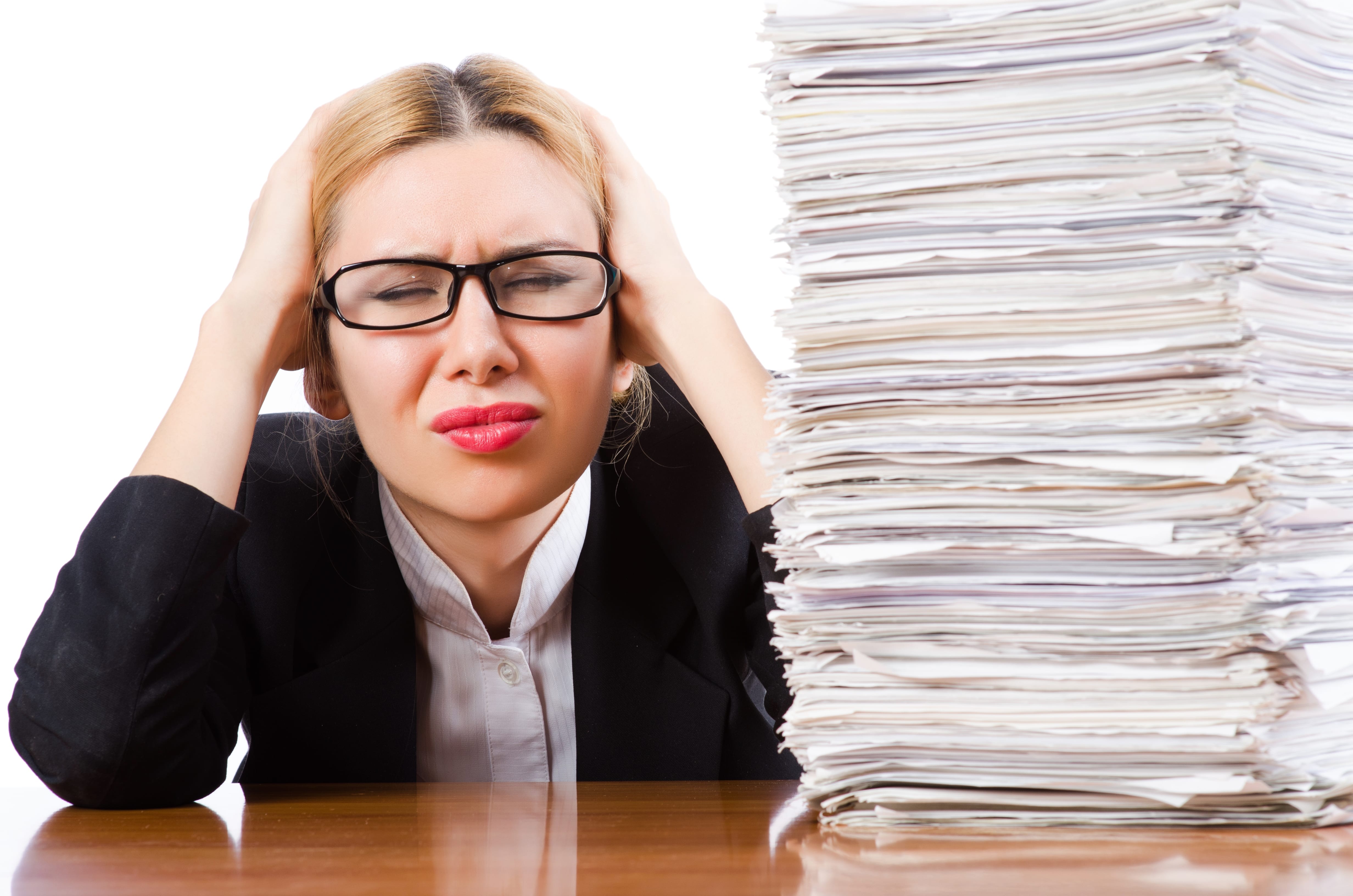A huge stack of white papers next to a woman holding her head. She has tremendous dental front desk stress.