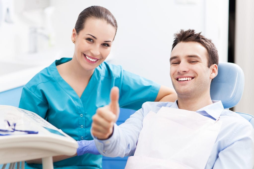 The Dental Hygiene Schedule Master Class Teaches How To Create & Maintain The Ideal Dental Hygiene Schedule. A dental hygienist sits with a male dental patient in the dental office.