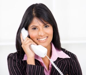A smiling woman answers a dental office telephone. She has great dental office customer service as she focuses only on her patient calling.