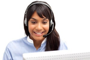 A smiling woman wearing a headset answers the telephone and is working on the computer. She is providing the best dental office customer service.