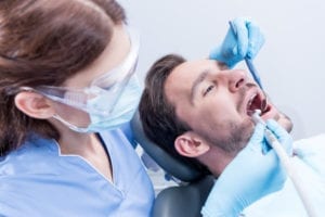 A dental hygiene patient is having his teeth cleaned by a dental hygienist. Dental office hygiene reactivation keeps dental patients coming back to the office when they are due.