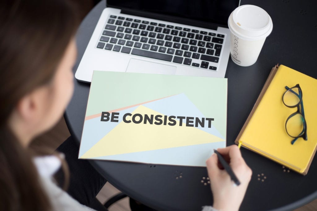 It is important that the dental office is consistent in managing their hygiene reactivation systems. A woman sits at her computer with a note in front of her that says " Be consistent" Dental office hygiene reactivation requires consistency.