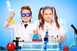 A young boy and girl stand in front of a science experiment. There is a science behind learning dental hygiene scheduling. 