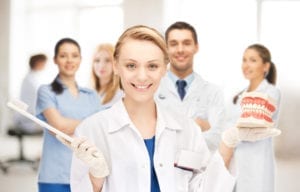 A group of dental clinicians stand together holding a toothbrush and models of teeth. Learning dental hygiene scheduling improves dental office productivity.