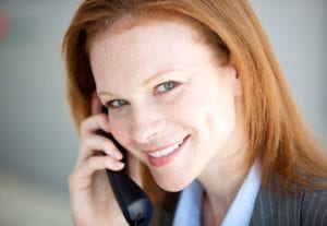 Building trust with dental patients often starts with "Hello" when dental patients reach out to the dental office for the very first time. A woman is answering the dental office telephone and smiles.