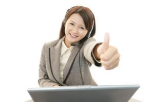 A woman with a headset smiles with a thumbs up as she is improving dental customer service she is having a better day.