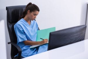 A dental front office team member sits at her desk and writes in a folder. She works on inactivating patients who haven't been into the dental office in the past 18 months.
