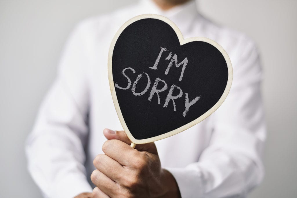 A man holds a chalkboard heart that says "I'm sorry" to represent apologizing to a dental patient with a complaint.