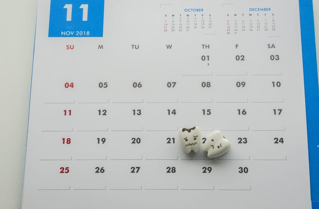 A tooth rests on a calendar representing that it is time for a hygiene visit to the dentist.