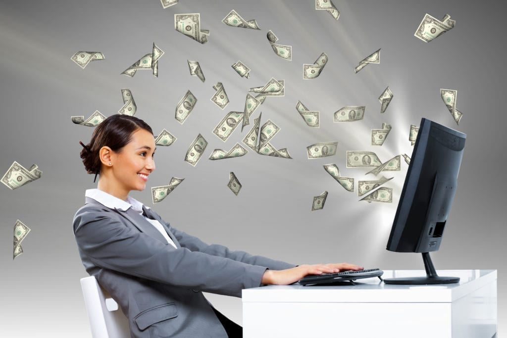 A dental front office team member sits at her computer and smiles as money flies from her screen. Working her dental office weekly reports generated more money for her dental practice.
